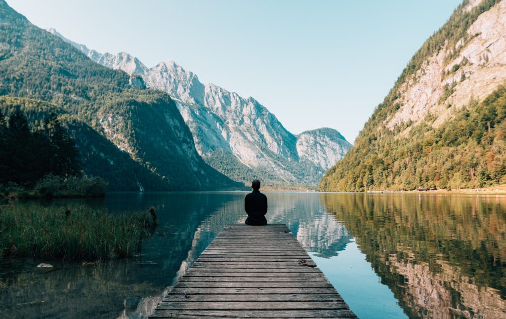 Individual is looking out into nature of a lake with mountains.