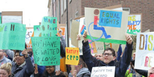 A group of Disability rights protesters gather in Ireland to call for the ratification of the United Nations’ Convention on the Rights of Persons with Disabilities (CRPD). From left to right, the signs held by protestors read: “We have the right … education” “Why have we waited so long” “Ratify CRPD” “Equal rights” with an image of the international symbol of access “Ratify the UNCRPD”