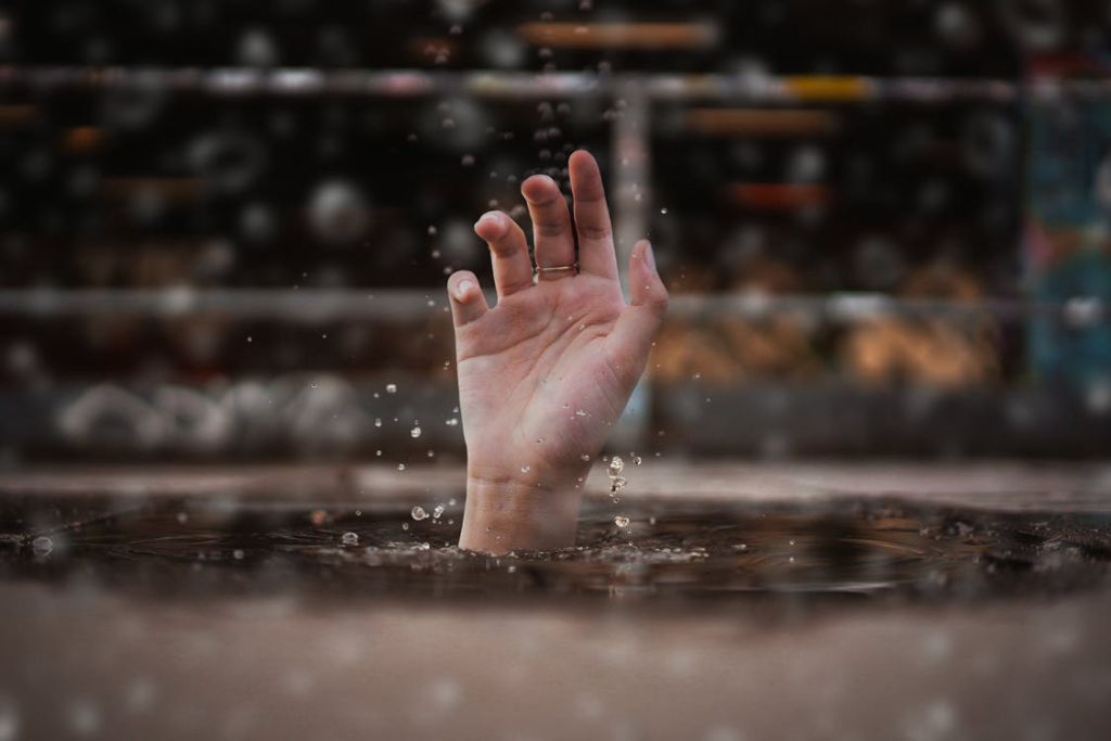 Person drowning in water and reaching a hand out. 