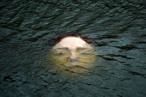 A life-like face of a woman almost completely submerged in water.