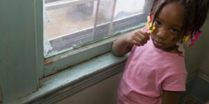 Four-year-old Taharah Abdulhaqq stands by a window in her home, where lead-based paint chips from the wood.