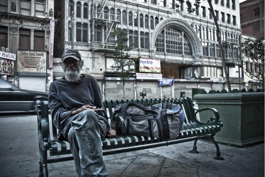 Unhoused man sitting on a bench next to a busy street