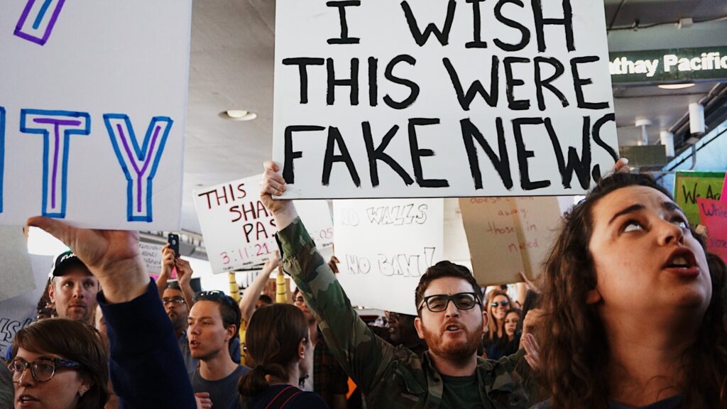 In a crowd of protesters, a man holds a sign up that says: "I wish this were fake news"