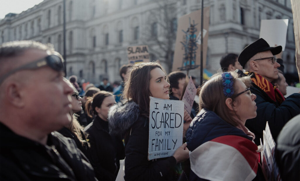 young woman in an outdoor crowd holding a sign that says "I am scared for my family" #SaveUkraine